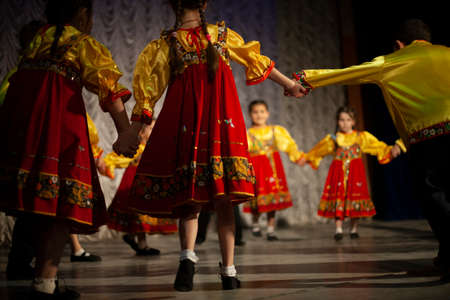 Children in folk costumes lead a round dance. Performance on stage. Folk dance lessons.の写真素材