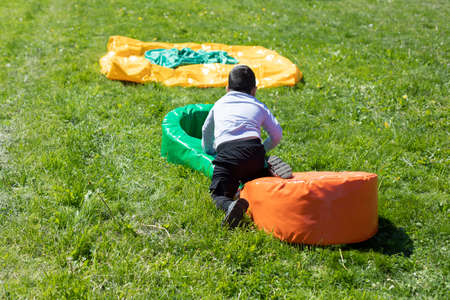 The baby's playing in the yard. Children's summer holidays. A sports obstacle for a preschooler. The boy jumps over a soft poof on the lawn.の写真素材