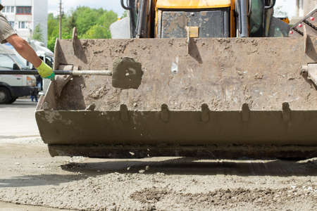 Work with a shovel at a construction site. A worker throws cement and gravel with a shovel. Cleaning the road from scattered building material.の写真素材