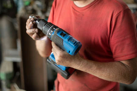 The man shows a screwdriver. A guy in a workshop with a power tool in his hand. A middle-aged man is showing his instrument.の写真素材