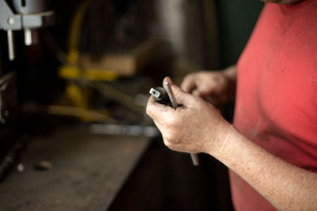 A man pulls out a drill. Installing a drill for a drill. Works in the garage. The master's hands hold the part of the electrical equipment for drilling. Fixing the steel part.の写真素材