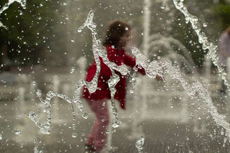Children run among the jets of water. Droplets of liquid fly in the air. Rest of children in summer in the park.の写真素材