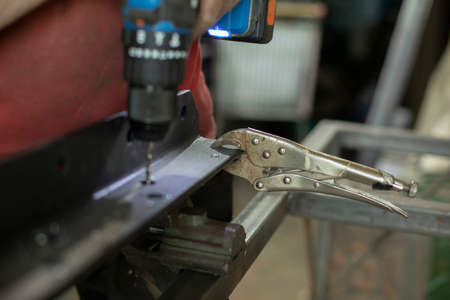 A man drills holes in the metal. The guy works in the garage. Hard man's work. Drilling holes a blank.の写真素材