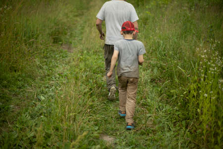 The child walks with his father across the field. Man among plants. A schoolboy with an adult man go to look for berries.の写真素材