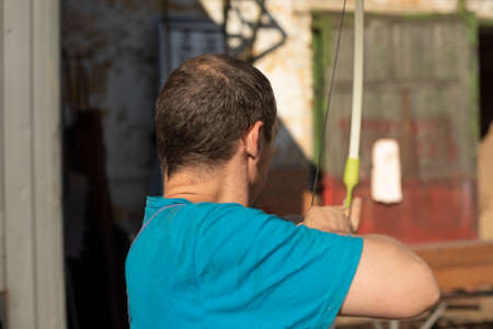 Archery. The man tries to shoot an arrow. A guy in work clothes is playing with a bow.の写真素材