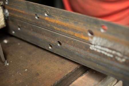 Drilled holes in the metal. Work in a metal workshop. The hand holds a steel blank. A man works in the garage.の写真素材