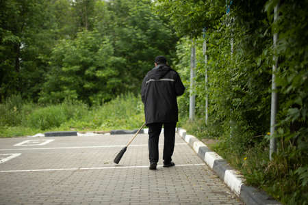 The janitor sweeps the street. Cleaning up in the parking lot. The guy's cleaning up the dirt with a broom. Putting order on the street. Cleaning the surface of the debris.の写真素材