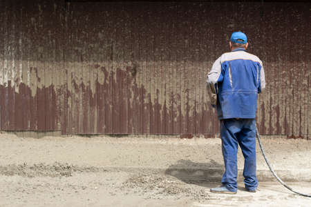 A man washes the fence with a hose. The builder cleans the fence from dirt. Cleaning at a construction site.の写真素材