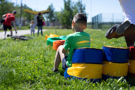 The boy is sitting on the playground. A child on a soft ottoman. Child in the summer on the street. The boy is tired of playing.の写真素材