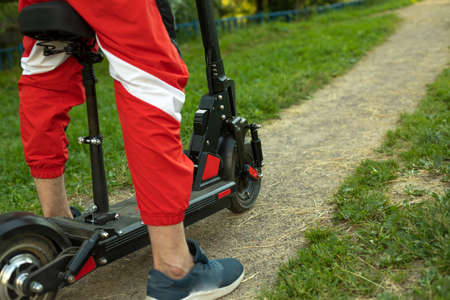 Electric scooter in the park. The guy is getting ready to go by electric transport. Legs on the scooter platform.の写真素材