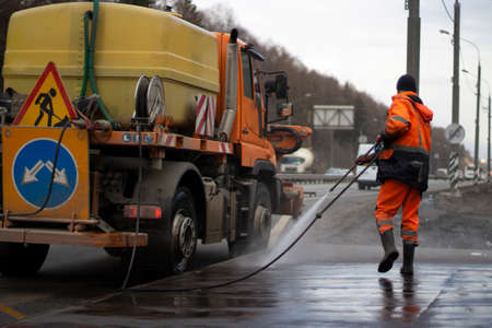 Sanitary handling of the bus stop. A man washes the road with a jet of water from a hose. A worker disinfects a public place. A water machine and a man.の写真素材