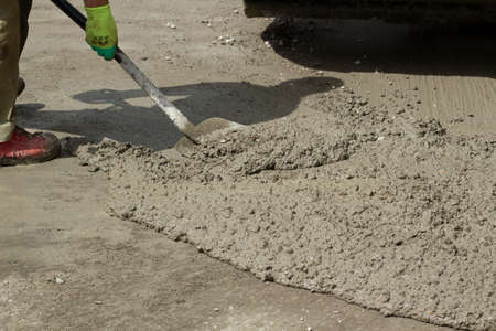 Cleaning the mortar with a shovel from the road. Clearing the road of spilled cement. A shovel in the hands of a worker.の写真素材