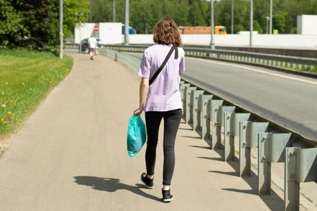 The girl walks down the road. A woman in a T-shirt in the summer. A man walks along the highway.