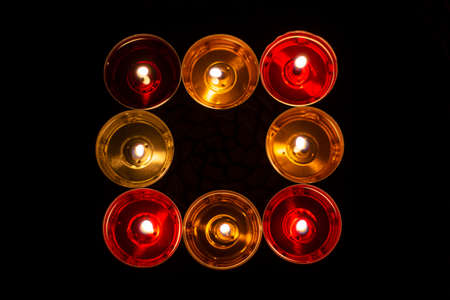 Square of candles. Candles burn in the dark. Orange wax and red wax. Eight candles evaporate from heating.の写真素材