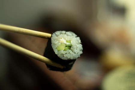 Sushi holds with sticks. Sushi with rice and cucumber. Asian cuisine. Fresh food.の写真素材