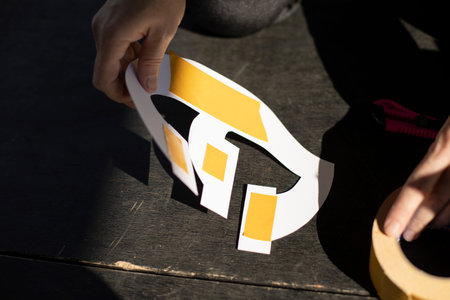Cutting the adhesive tape. Work with a conceler knife. A person glues a paper figure. Hand work.