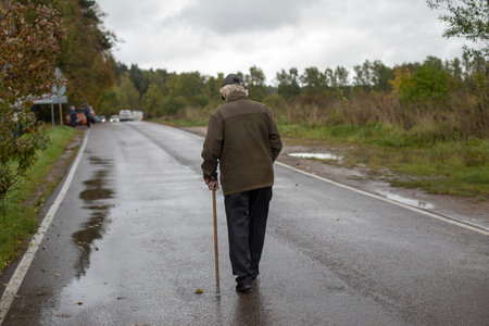 Old man walks down road. Pensioner with stick for support. Man with leg injury. Grandpa in Russia...