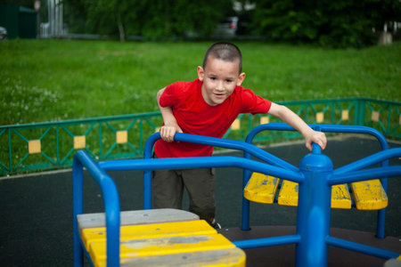 Child on merry-go-round. Boy spins on carousel for children on playground. Junior schoolboy plays...
