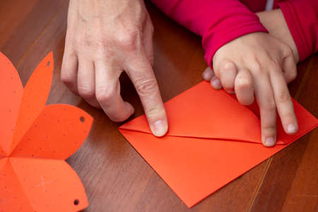 Folding paper. Lesson in children's creativity. Child and adult create envelope together. co-creation. Origami background in progress.の写真素材