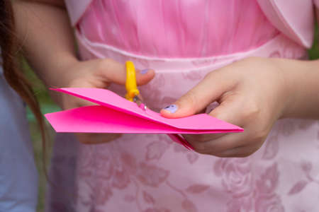 Cutting from colored paper. Details of master class. children's creativity. Needlework lesson. Child cuts pink paper with scissors. Making origami.の写真素材