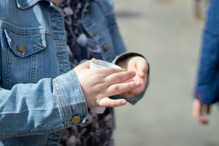 Child holds glass for money. Collecting small things in plastic cup. Child in denim clothing. boy's...