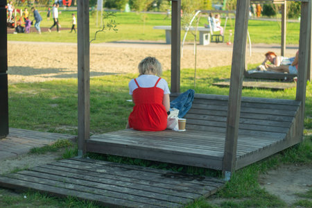A little girl sits on a wooden swing in the park and drinks coffee.