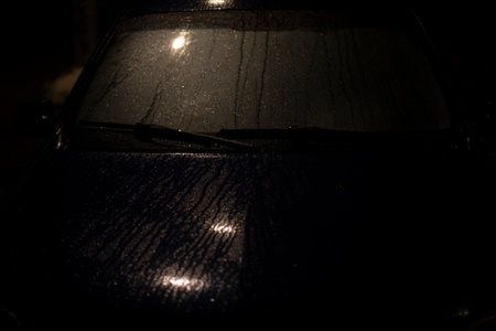 Raindrops on car in dark. Car at night in parking lot. Car in rain. Overnight parking detail.の写真素材