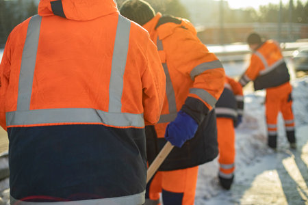Workers remove snow with shovels. Workers in orange suits. city cleaning service. Snow removal details.の写真素材