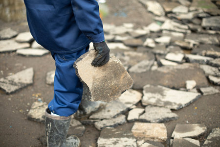 Worker carries stone. Cleaning of construction waste. broken stone. Man collects cobblestones on road.の写真素材