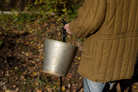 Grandfather with bucket of water. Old man carrying bucket. Grandpa in the garden. Life of pensioners in Russia.の写真素材