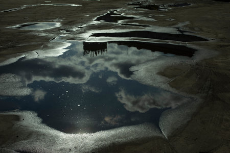 Puddle on pavement. after rain. Road in pits. Reflection of sky in puddle.