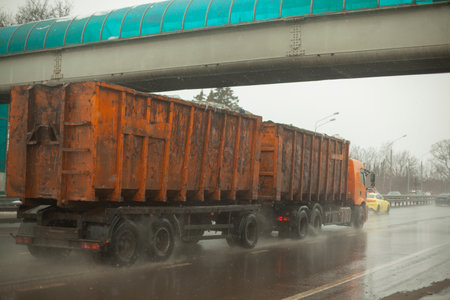 Truck with orange body. big trailer. Transportation of waste. fuel delivery. Passage under bridge. rain on highway.の写真素材