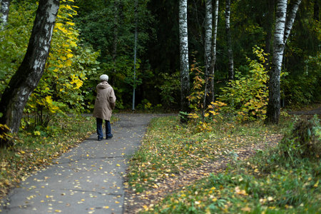 Old woman in park in fall. Pensioner walks through autumn forest. grandma walk path. Walk down street.の写真素材