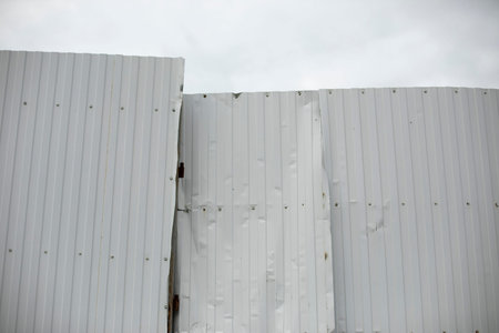 Broken steel profile fence. Wrinkled metal fence. White steel barrier. Tinted iron.の写真素材