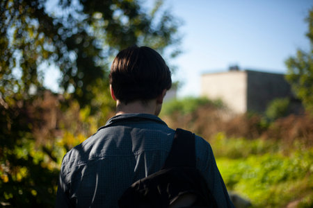 Guy walks through woods. Man from behind in summer. Young man came to village. Details of walk on sunny day.の写真素材