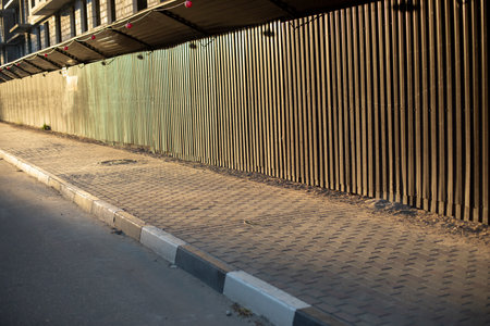Fence along road. Fencing of construction site of house. Brown steel profile. Marking on curb. Tile track.の写真素材