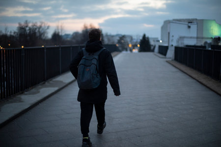 Guy walks across the bridge in the evening. Man in town at night. Man with backpack in black clothes. Suspicious person.の写真素材