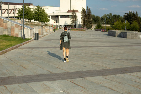 Girl walks through square in summer. Walk around city. Girl with small backpack. City is in summer.の写真素材