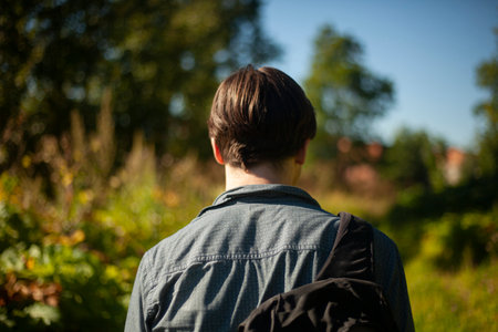 Guy walks through woods. Man from behind in summer. Young man came to village. Details of walk on sunny day.の写真素材