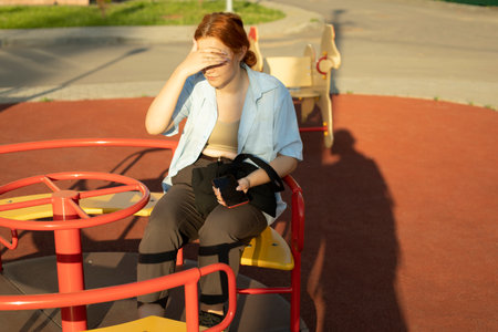 Girl sits on playground. school girl on carousel. Teenagers in summer. Student waits on swing.の写真素材