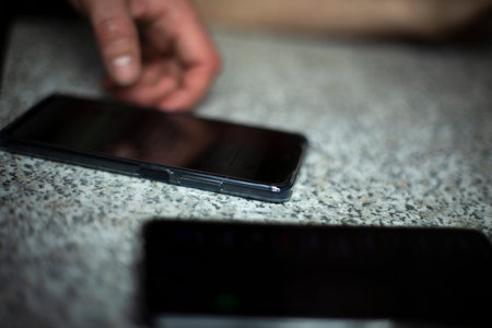 Smartphone on table. Two black phones. Hand reaches for smartphone.