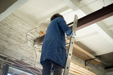 Guy is standing on stairs. Worker hangs chain on steel beam. construction staircase. Man stands at...