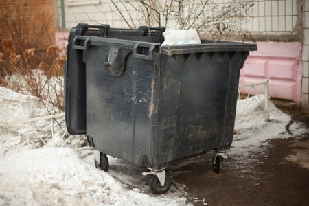 Black garbage can on street. Dirty container in ghetto. Waste garbage. Container on wheels.の写真素材
