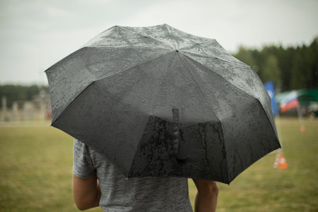 Black umbrella in rain. Large umbrella in bad weather. Man on street on cloudy day. Details of walk.