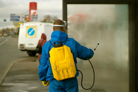 Guy washes bus stop. Worker with canister of water. Spraying detergent on glass. Laundering of urban infrastructure.の写真素材