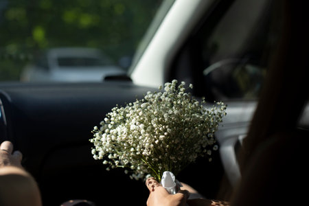 Bouquet of flowers in car. Bride's bouquet is in hands of girl. White flowers in hand. Gift to girl.の写真素材