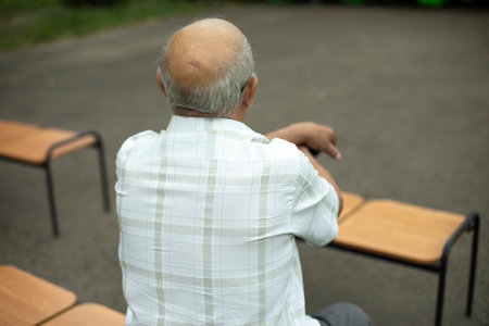 Old man sitting on bench. Bald spot on head. Elderly man at street concert. Man without hair.の写真素材
