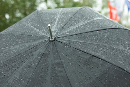 Black umbrella in rain. Large umbrella in bad weather. Raindrops on black material. Grass umbrella on street.の写真素材