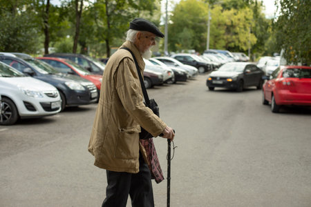 Old man walks through parking lot. Old man with stick. Man in poor clothes. Retired in Russia. Russian old man.の写真素材