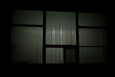 Big window at night. window in building. Blinds cover light of lamp. House is outside.の写真素材